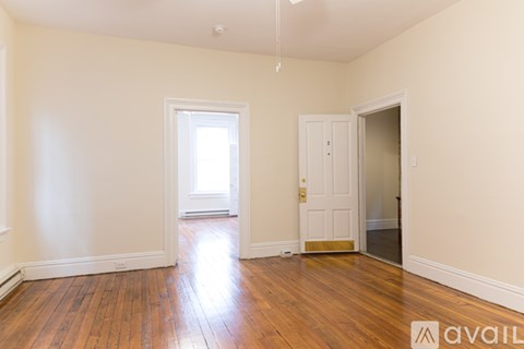 A room with wooden floors and white walls, with a door on the right side.