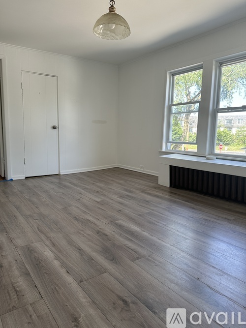 A room with wooden flooring and a window showing trees outside.