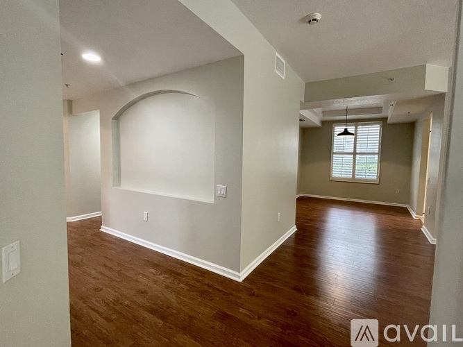 A spacious room with wood flooring and a large arched window.