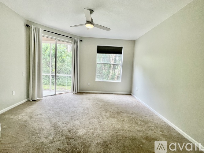 A room with a carpeted floor, a ceiling fan, and a window with a view of trees.