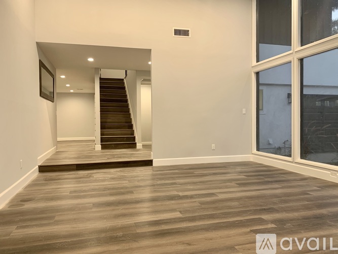 A spacious room with wooden flooring and a staircase leading to another level.