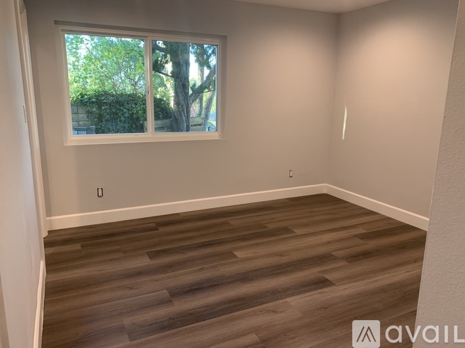 A room with wooden flooring and a window showing trees outside.