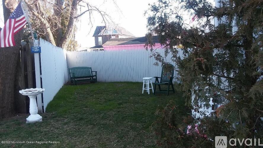 A white birdbath sits on a lawn in front of a white fence.