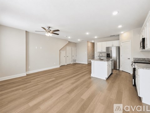 A spacious kitchen and living room with wooden flooring and white walls.