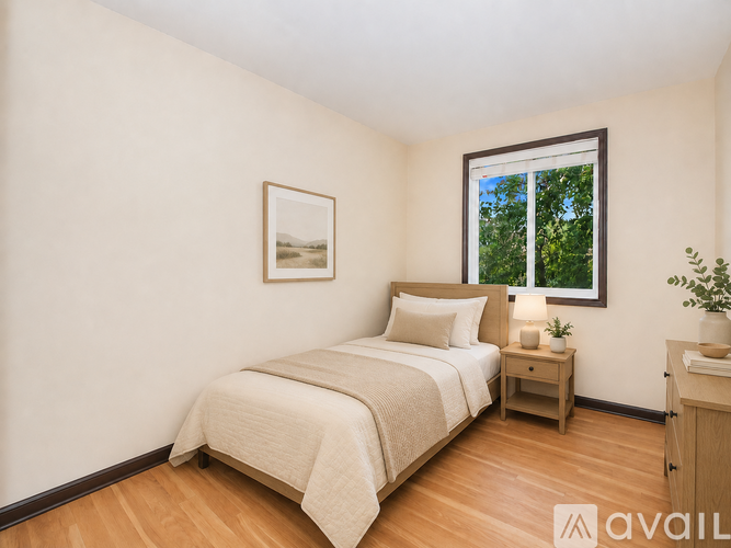 A bedroom with a bed, nightstand, and a window with a view of trees.