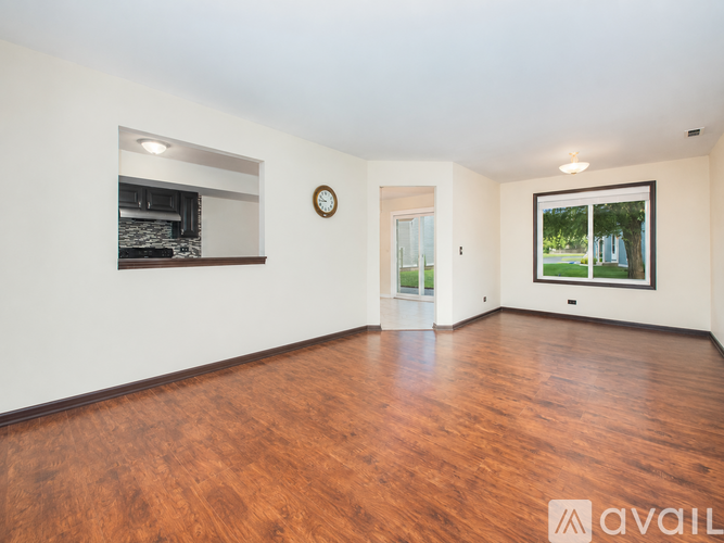 A spacious room with wooden flooring and a large window overlooking a green area.