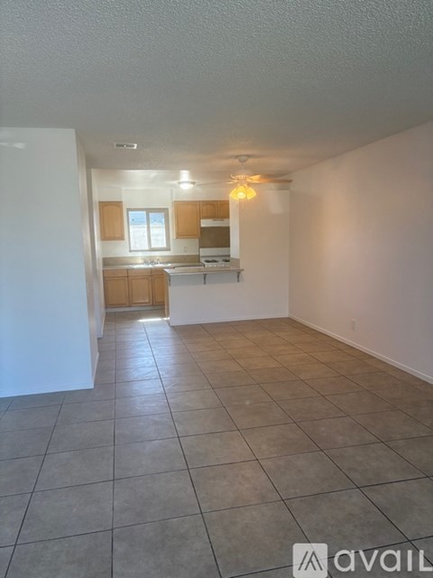 A spacious room with tiled flooring and a kitchen area in the background.