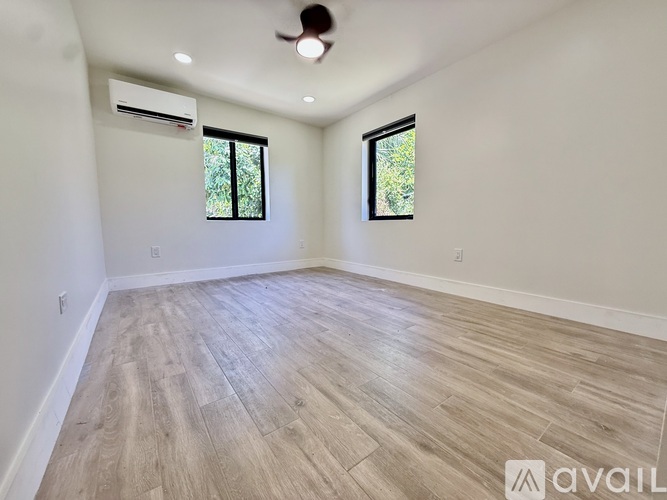 A spacious room with wooden flooring and two windows.