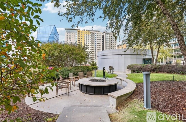 A park with a circular structure surrounded by trees and buildings in the background.