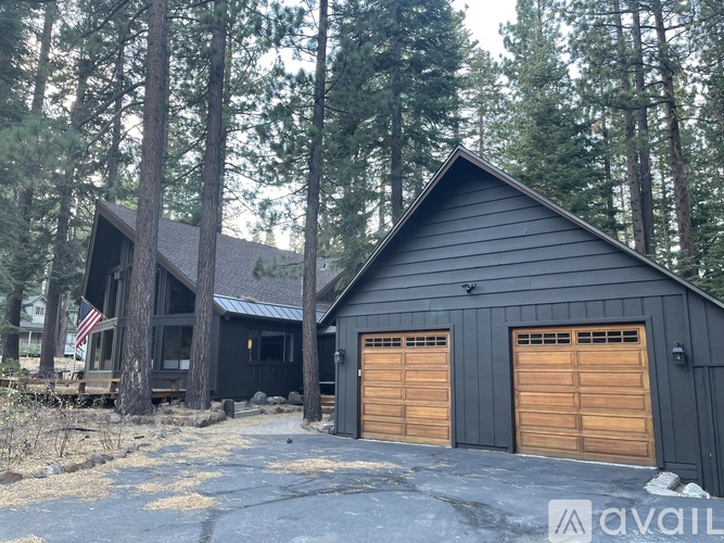 A black house with two garage doors is surrounded by trees.