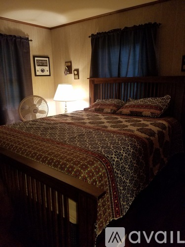 A bedroom with a bed, a fan, a lamp, and pictures on the wall.