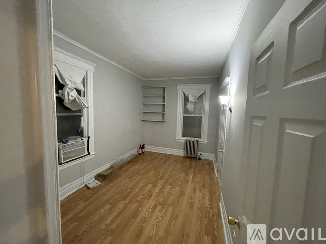 A room with wooden floors and white walls, with a window and a radiator.