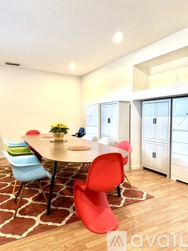 A dining room with a round table surrounded by chairs in different colors.