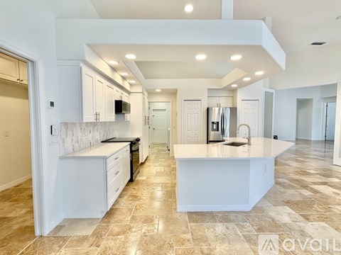 A spacious kitchen with white cabinets and a marble backsplash.