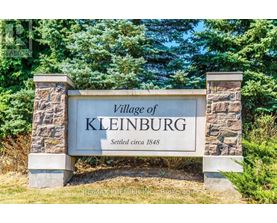 A stone sign that says Village of Kleinburg is in front of trees.