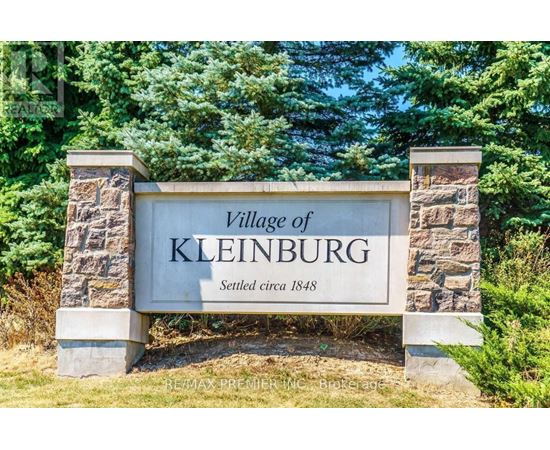 A stone sign that says Village of Kleinburg is in front of trees.
