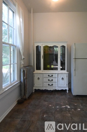 A white cabinet with glass doors and drawers is in a room with a window and a radiator.
