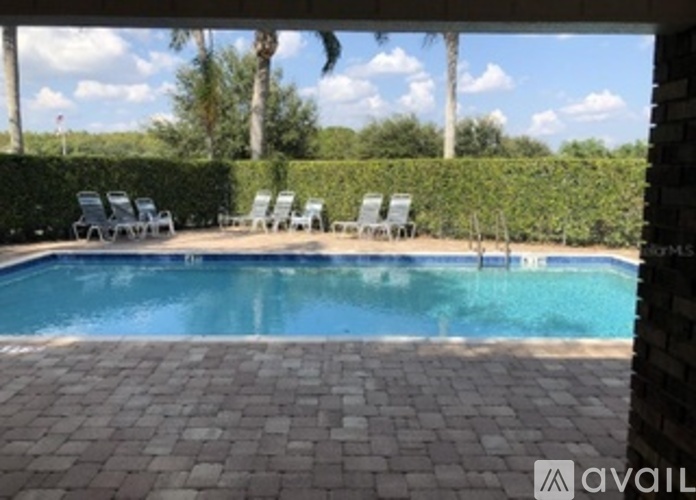 A pool surrounded by a brick patio and lounge chairs.
