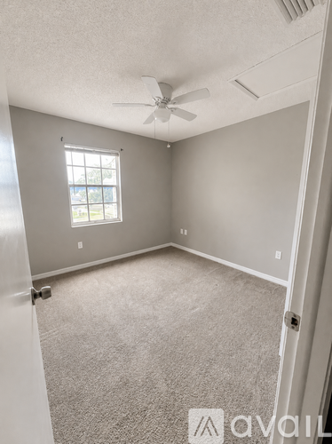 A room with a carpeted floor, a ceiling fan, and a window with a view of trees.