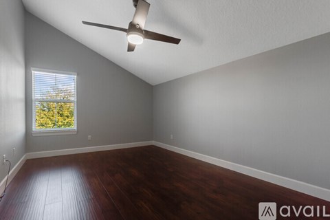 A room with a ceiling fan and a window showing trees outside.