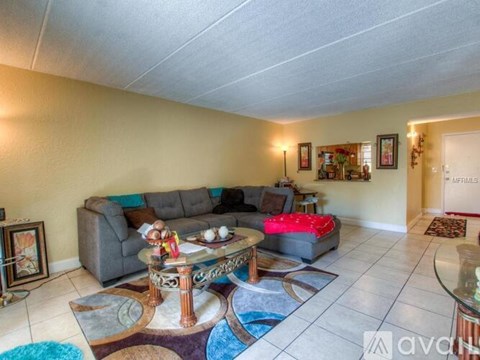 A living room with a grey couch, a glass table, and a red ottoman.