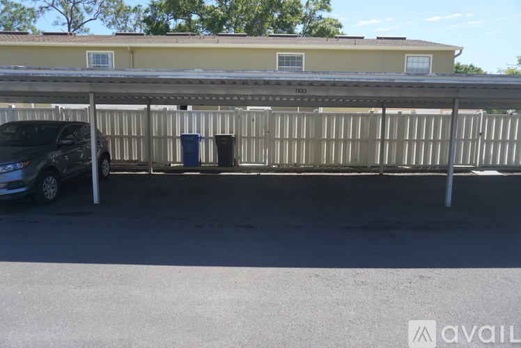 A car is parked under a metal structure with a building in the background.