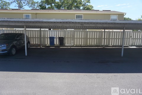 A car is parked under a metal structure with a building in the background.