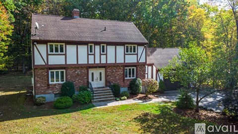 A house with a white and brown facade is surrounded by greenery.