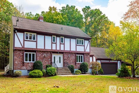 A house with a red brick facade and white trim is surrounded by trees and grass.