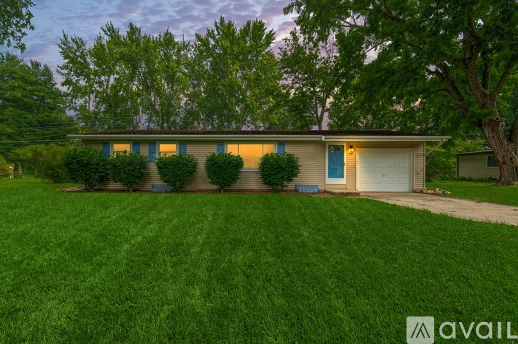 A house with a blue door is surrounded by greenery and has a well-maintained lawn.