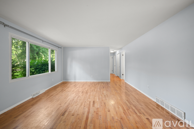 A room with wooden flooring and a window overlooking trees.
