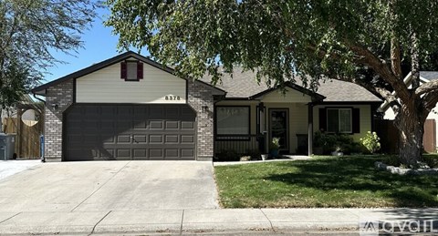 A house with a garage and a tree in front.