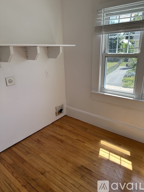 A room with wooden floors and a window showing a view of a driveway and trees.