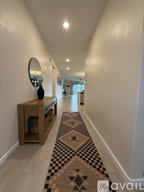 A hallway with a checkered rug and a mirror on the wall.
