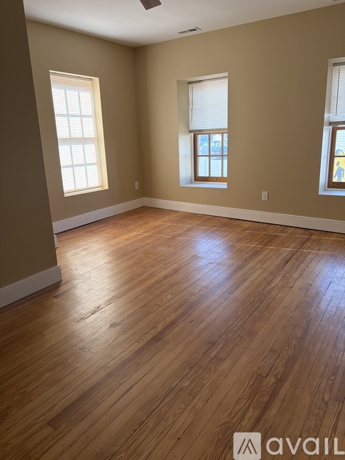 A room with wooden flooring and three windows.