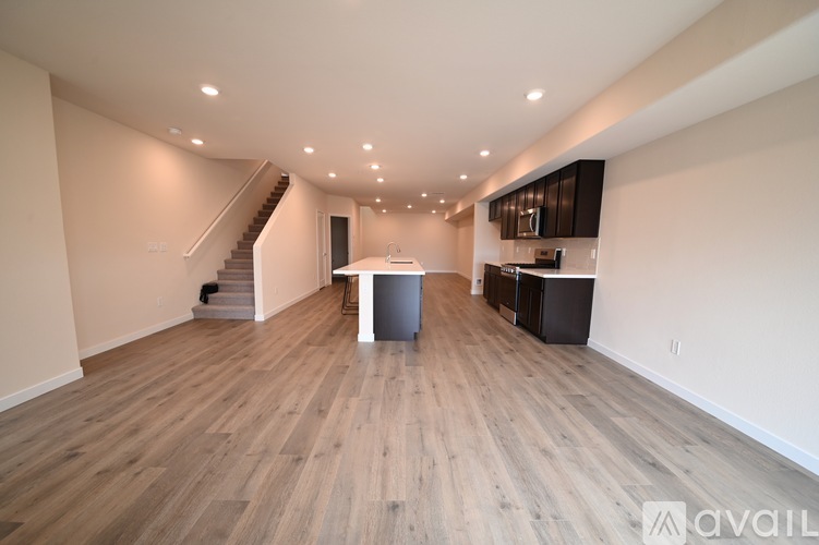 A spacious living room with wooden flooring and a staircase in the background.