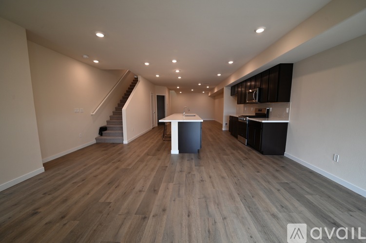 A spacious room with wooden flooring and a staircase on the left side.