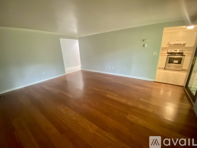 A room with wooden flooring and a kitchen in the background.