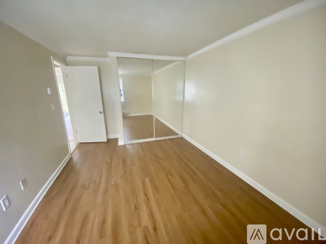 A room with wooden flooring and white walls, with a door and a window.