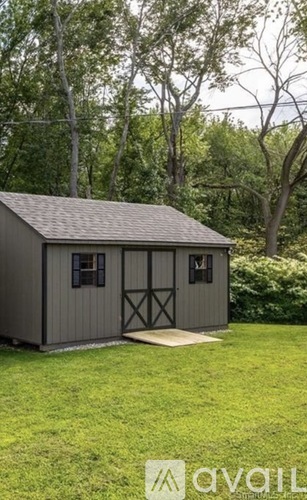 A shed with a grey roof and black doors is situated in a grassy area.