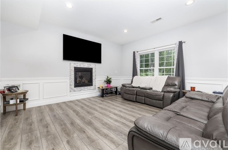 A living room with a grey leather couch and a black screen on the wall.
