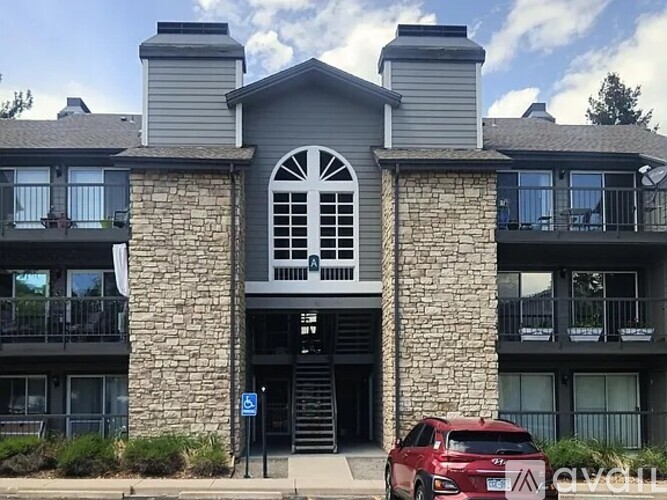 A red car is parked in front of a stone building with a balcony.