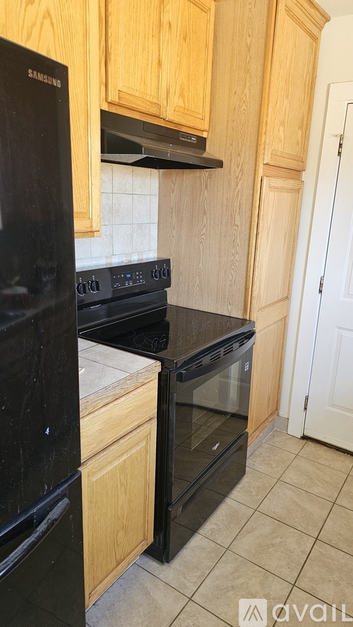 A black Samsung refrigerator in a kitchen with wooden cabinets.