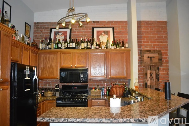 A kitchen with a black refrigerator and a brick wall.
