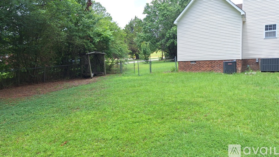 A grassy yard with a house and a fence in the background.