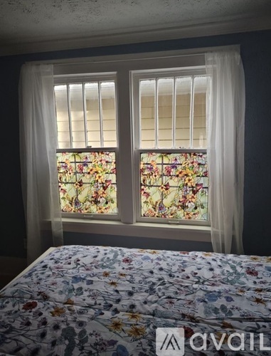 A bedroom with a floral bedspread and a window with floral stained glass.
