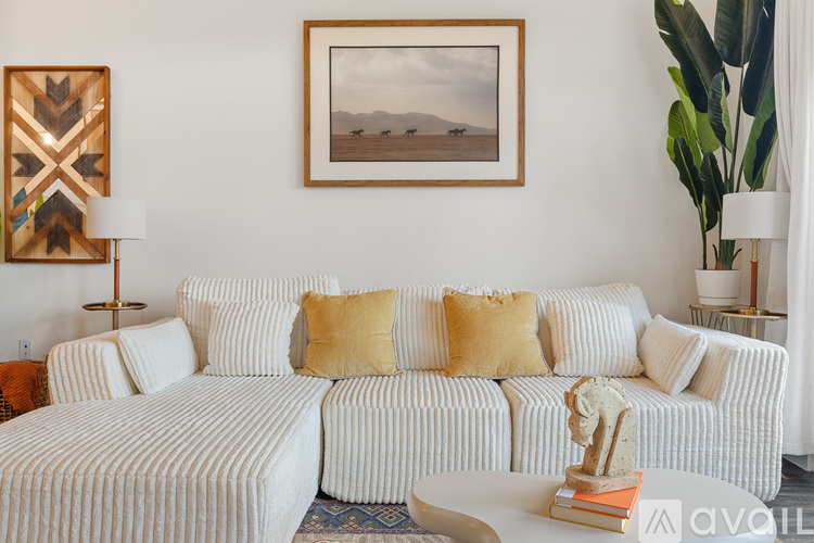 A living room with a white couch and a painting on the wall.