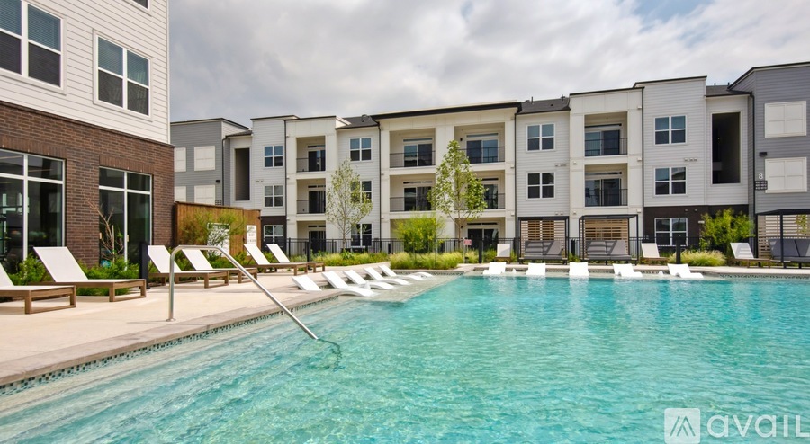 A swimming pool in front of apartment buildings with lounge chairs on the side.