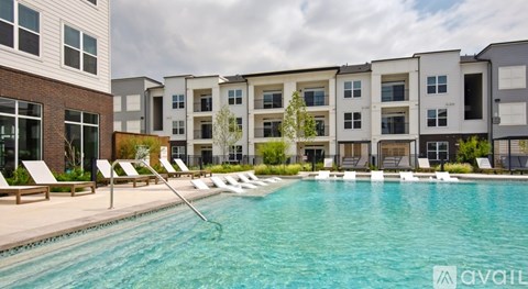 A swimming pool in front of apartment buildings with lounge chairs on the side.