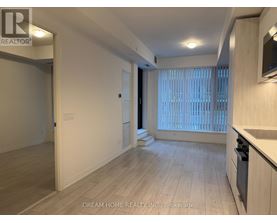 A spacious room with wooden flooring and a kitchen area with white cabinets.